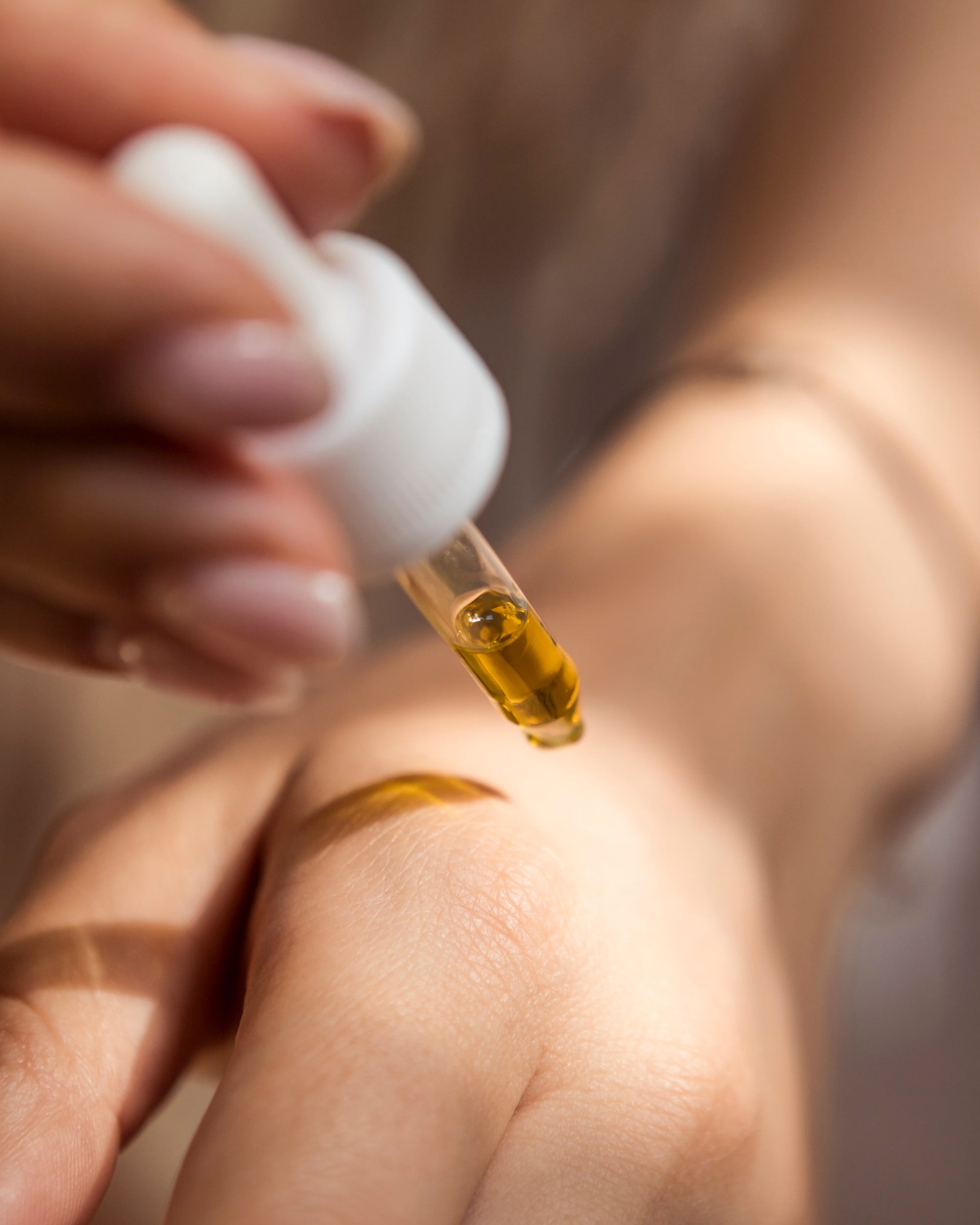 Hand hält Pipette und tropft Öl auf die Haut