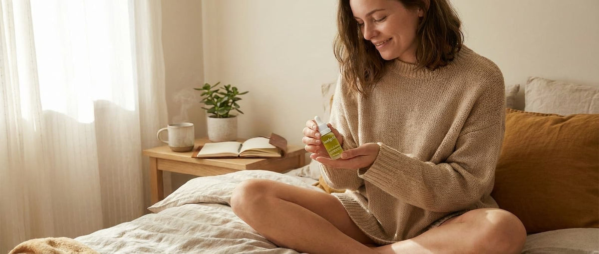 Junge Frau mit PMS auf dem Bett mit CBD Öl in der Hand 